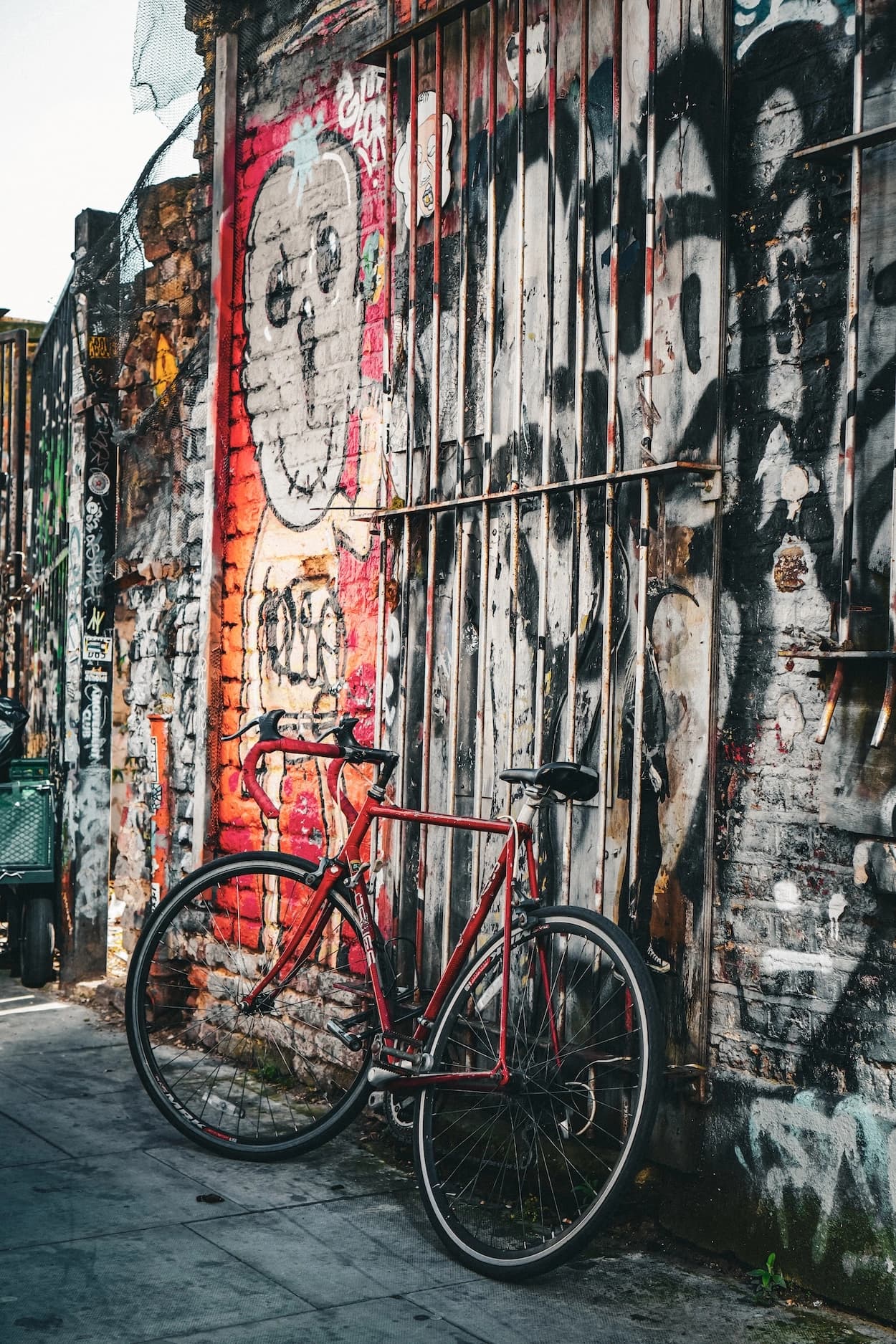 A red road bike leaning against a graffiti-covered brick wall and boarded window on a London side street